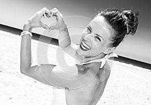 Happy modern woman on seashore showing heart shaped hands