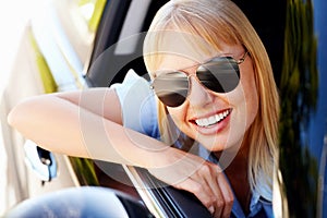 Happy modern woman sitting at the window of a car. Cute female wearing aviators sitting at the window of a car and