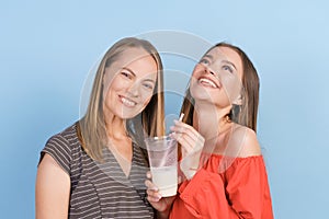 Happy mom and adult daughter drink milkshakes and laugh merrily in dresses