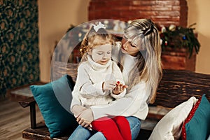 Happy mom and baby daughter reading having fun by the fireplace on Christmas or New Year's Eve. Parenthood