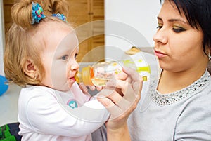 Happy mom and baby girl drinking from bottle. The concept of childhood and family. Beautiful Mother and her baby