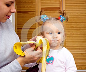 Happy mom and baby girl eating banan. The concept of childhood and family. Beautiful Mother and her baby