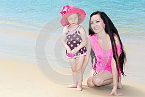 Happy mom and child girl hugging on tropical beach.