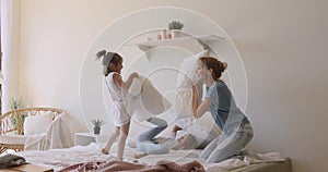 Happy mom and children daughters playing pillow fight on bed