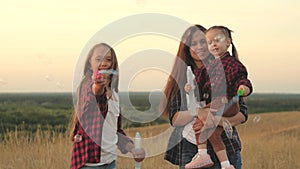 Happy mom and children play together, blow and catch soap bubbles. sisters play together in park at sunset. Happy family