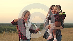 Happy mom and children play together, blow and catch soap bubbles. sisters play together in park at sunset. Happy family