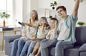 Happy mom, dad and children sitting on the sofa at home and watching television all together