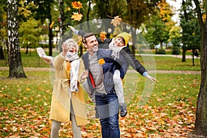Happy mom, dad and son having fun together in the autumn park, throwing golden leaves and laughing