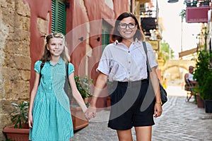 Happy mom and daughter child walking together holding hands along city street