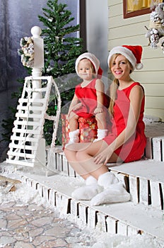 Happy mom and daughter in Christmas costumes are sitting under snow