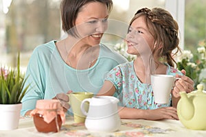 Happy mom and daughter drinking tea at home