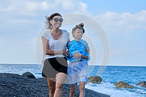 Happy mom and daughter kid hugging walking together along the beach