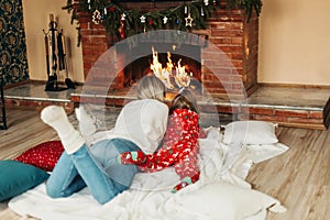 Happy mom and daughter are lying by the fireplace on Christmas or New Year& x27;s Eve. Rear view. Christmas mood, on the