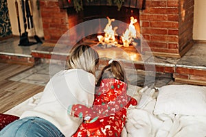 Happy mom and daughter are lying by the fireplace on Christmas or New Year& x27;s Eve. Rear view. Christmas mood, on the