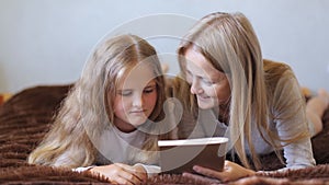 Happy mom and daughter are reading a book.Mother and daughter are lying and looking at a book