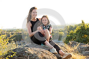 Happy mom and daughter relaxing on rocks in nature against the backdrop of the river. Happy Motherhood, Mother& x27;s Day