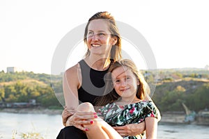 Happy mom and daughter relaxing on rocks in nature against the backdrop of the river. Happy Motherhood, Mother& x27;s Day