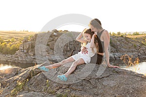 Happy mom and daughter relaxing on rocks in nature against the backdrop of the river. Happy Motherhood, Mother& x27;s Day