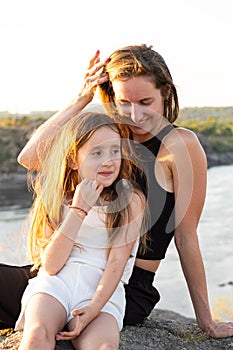 Happy mom and daughter relaxing on rocks in nature against the backdrop of the river. Happy Motherhood, Mother& x27;s Day