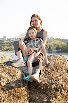 Happy mom and daughter relaxing on rocks in nature against the backdrop of the river. Happy Motherhood, Mother& x27;s Day