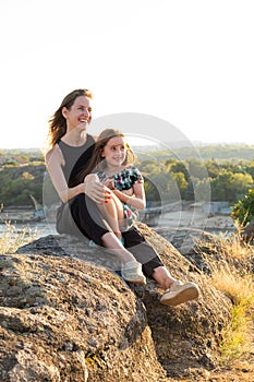 Happy mom and daughter relaxing on rocks in nature against the backdrop of the river. Happy Motherhood, Mother& x27;s Day