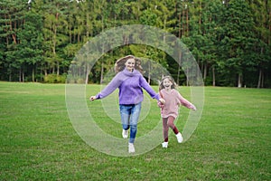 Happy mom and daughter run outdoors. Family vacation in nature. Joyful girl and woman have fun together