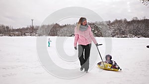 Happy mom and daughter sledding in winter in snow and playing snowballs. mother and child laugh and rejoice glide on an