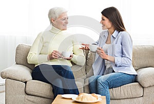 Happy mom and daughter talking and drinking tea