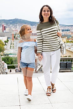 Happy mom and daughter walk along the street of European summer city