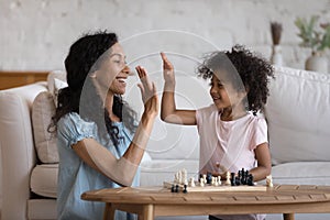 Happy mom giving high five to cute daughter over chessboard