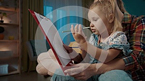 Happy mom helps her daughter draw with pencils while sitting on the living room couch close up. Daughter sits on mom