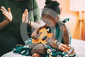 Happy Mom with her daughter playing guitar and singing together at home, happy family
