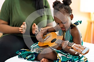 Happy Mom with her daughter playing guitar and singing together at home, happy family