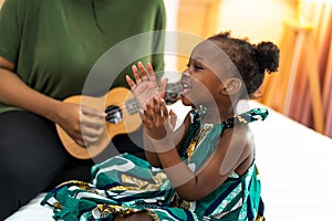 Happy Mom with her daughter playing guitar and singing together at home, happy family