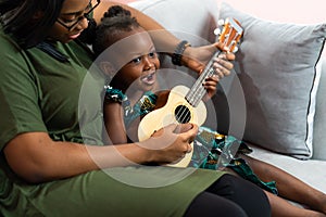 Happy Mom with her daughter playing guitar and singing together at home, happy family