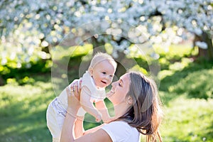 Happy mom, holding her cute baby boy in spring park