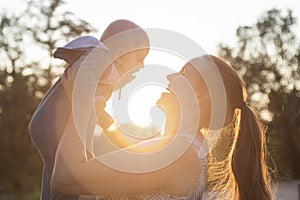 Happy mom holding her cute baby on sunset background. Backlight silhouette of a mother raising her kid at sunset with the sun in