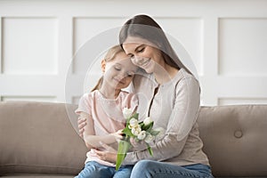 Happy mom hug little daughter thanking for presented flowers photo