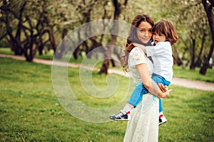 Happy mom hugs and kiss toddler kid son outdoor in spring or summer