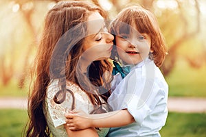 happy mom hugs and kiss toddler kid son outdoor in spring or summer. Loving family and mothers day