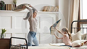 Happy mom and kid daughter having pillow fight on bed