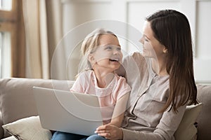 Happy mom and kid daughter laughing having fun with laptop