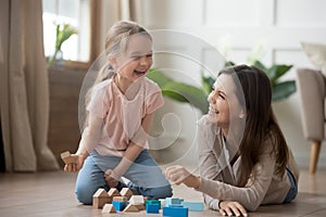 Happy mom and kid daughter laughing playing with wooden blocks