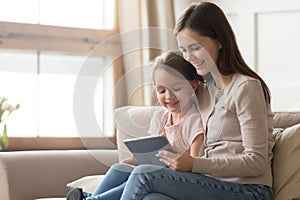 Happy mom and kid daughter using digital tablet on sofa