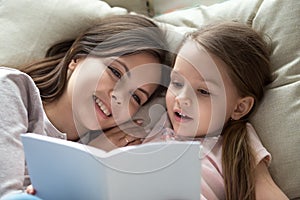 Happy mom listening child daughter learning reading book in bed