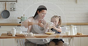Happy mom and little child daughter beating dough in kitchen
