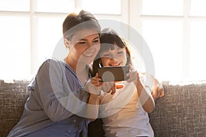 Happy mom and little child enjoy using smartphone at home