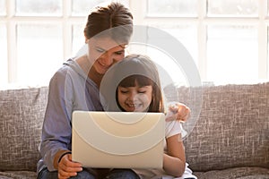 Happy mom with little daughter having fun online with laptop