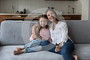 Happy mom and little daughter kid resting on home couch