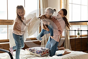 Happy mom and little daughters enjoying pillow fight on bed